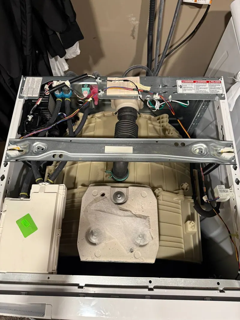 Top of the front-load washer opened up, with the tub, hoses and wiring in view