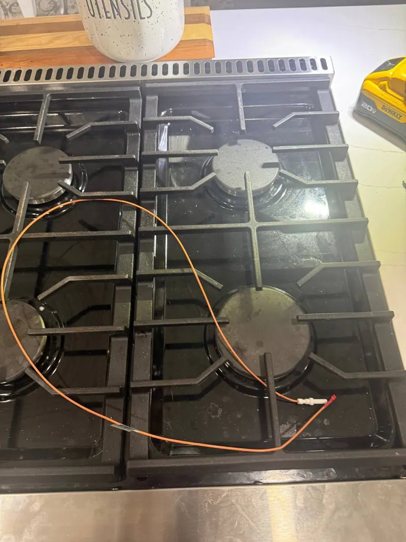 Burner igniter with an orange lead wire across the cooktop grates