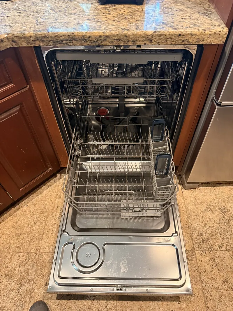 Open dishwasher with empty racks under a granite counter