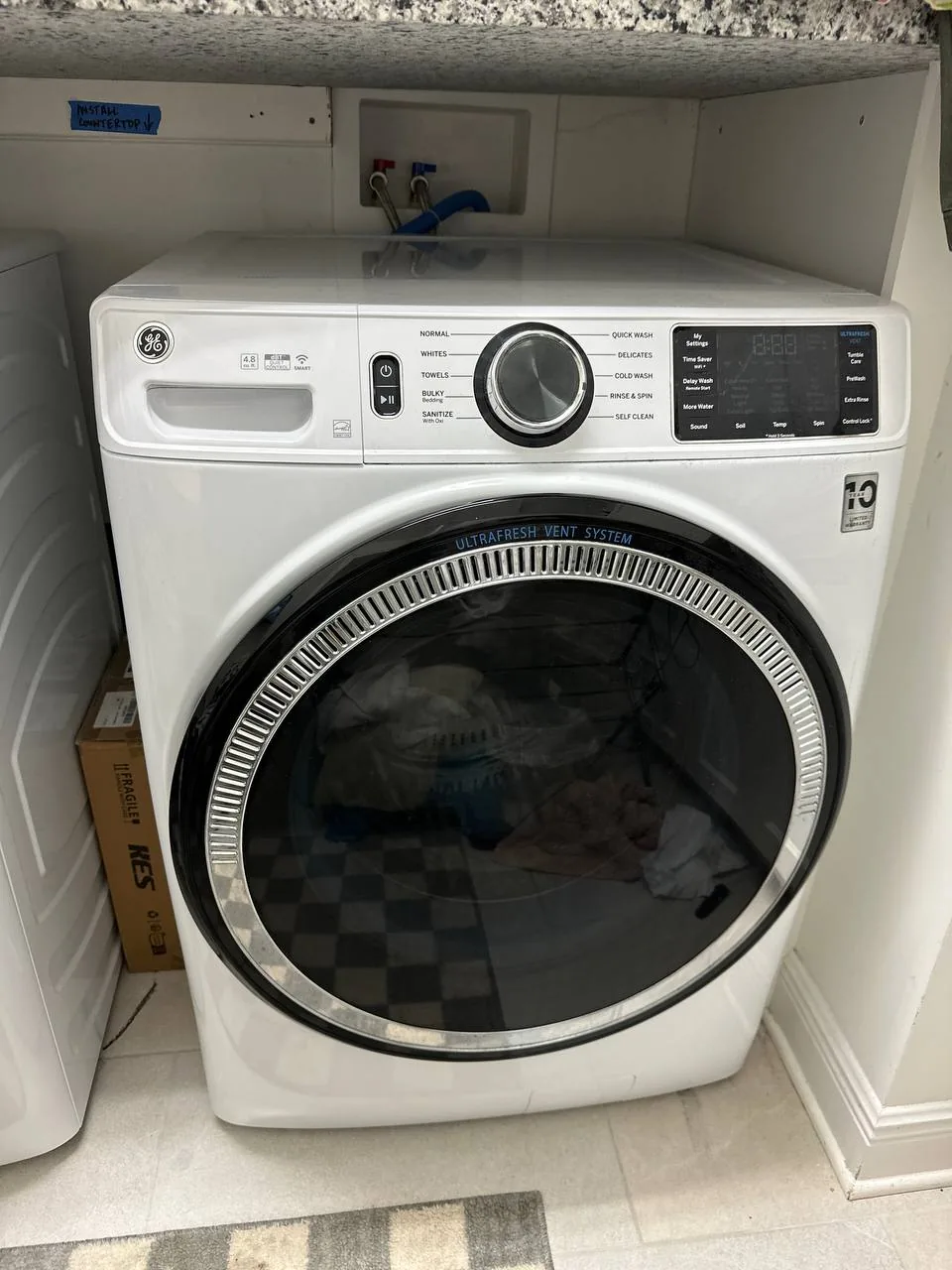 A white front-load washing machine, with the control panel visible and a small note about countertop installation above it