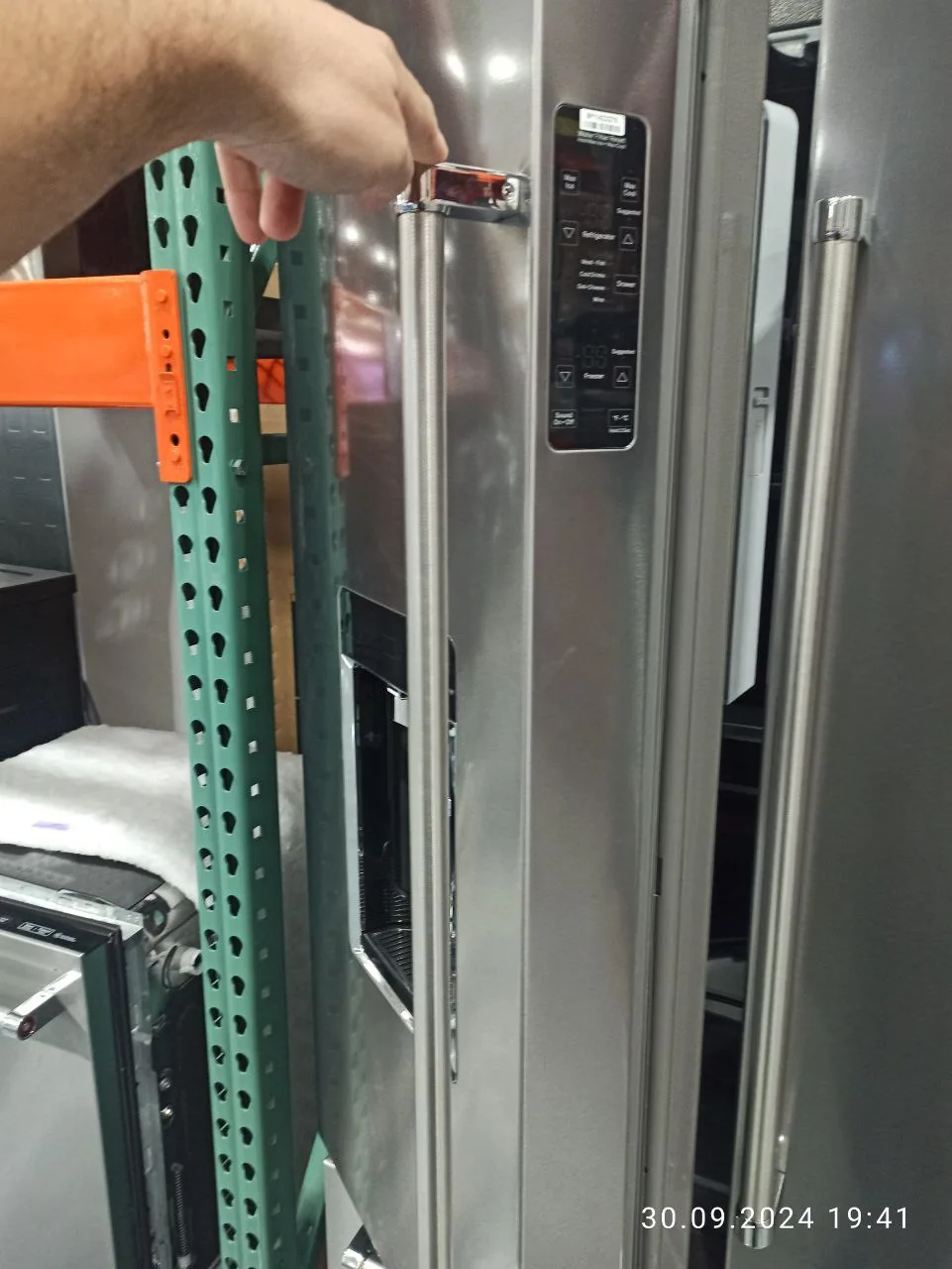 A technician's hand next to the control panel of a stainless steel refrigerator