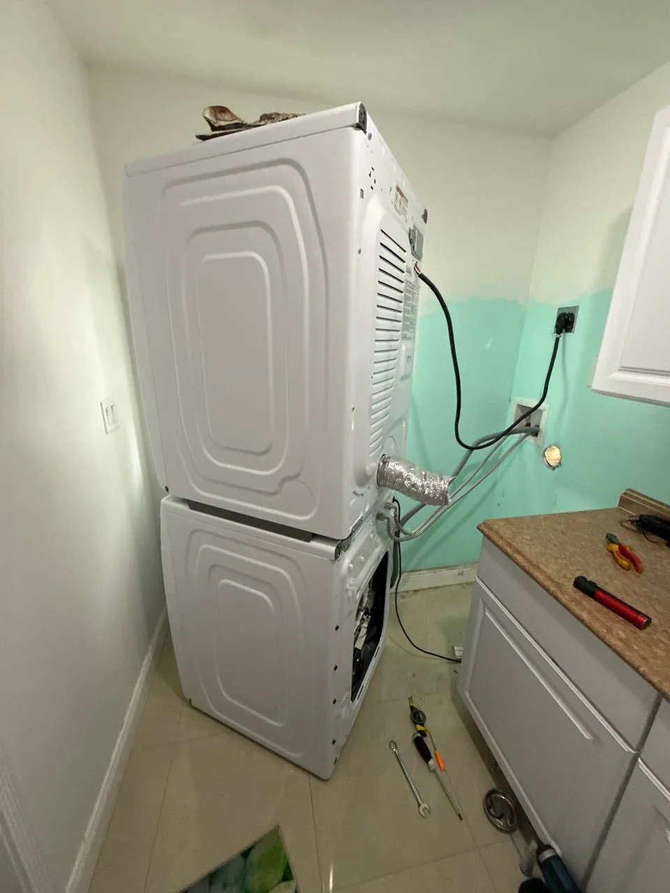 A stacked washer and dryer unit in a laundry room with tools on the floor and counter