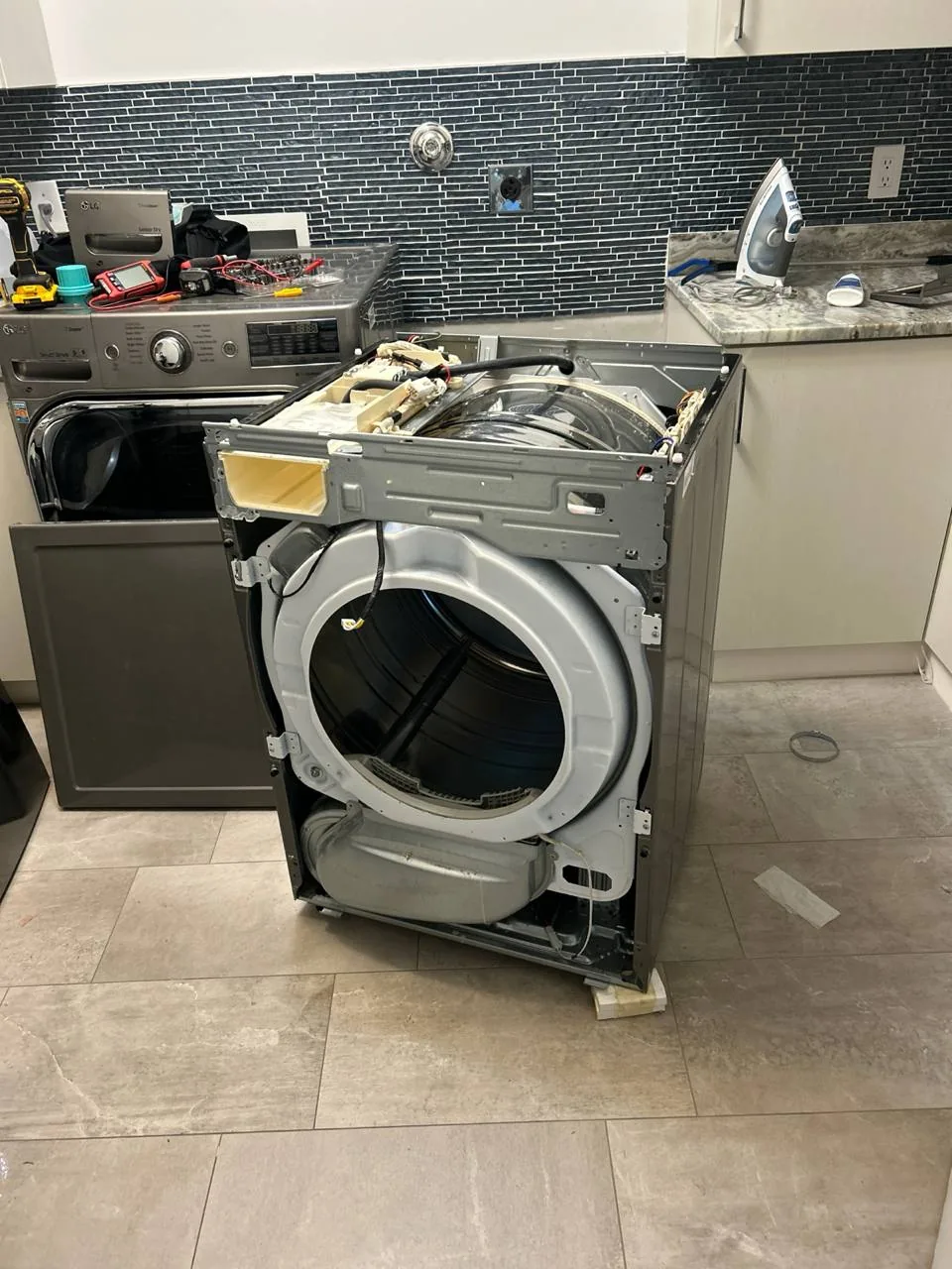 A disassembled washing machine in a kitchen setting with tools on the counter