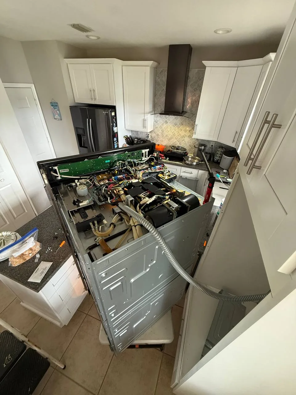 A dishwasher is pulled out from the counter and disassembled for repair in a kitchen