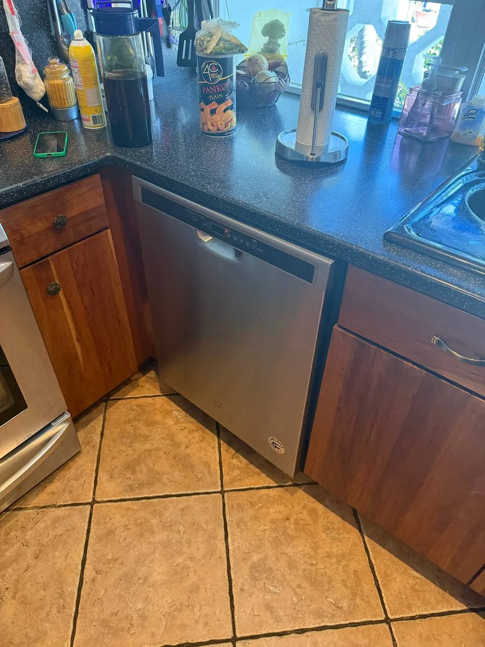 A stainless steel dishwasher is installed under a kitchen counter next to a sink