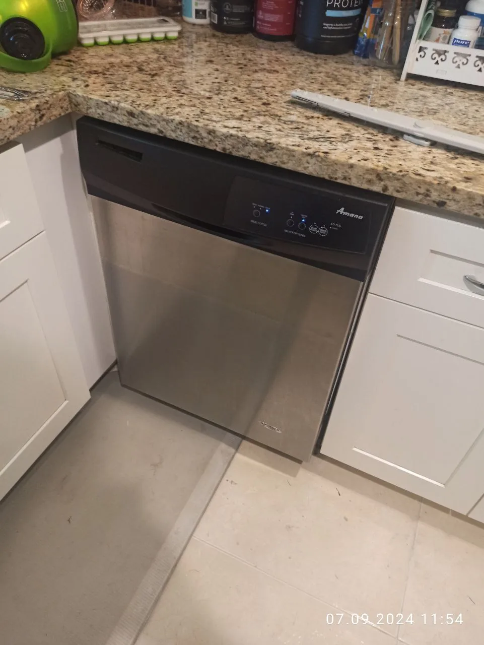 A stainless steel Amana dishwasher is installed under a granite countertop in a kitchen