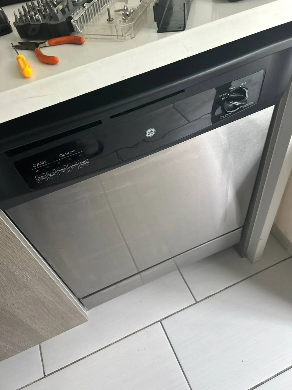 A stainless steel dishwasher with various tools on the counter above it