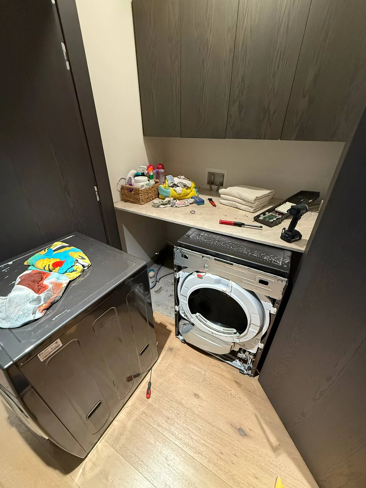 A disassembled washing machine in a laundry room with tools and cleaning supplies on the counter
