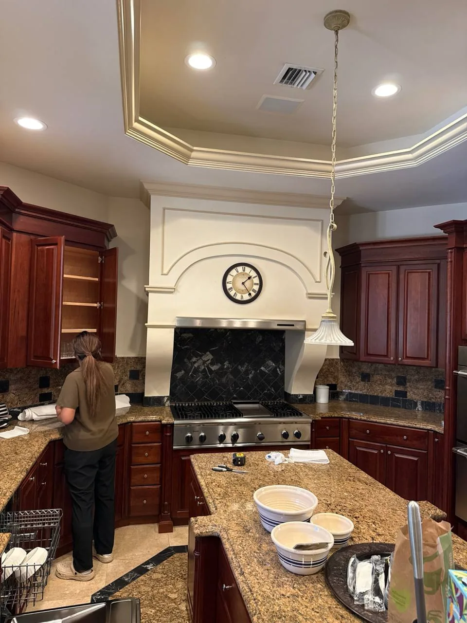 A technician is working on a cooktop in a kitchen with dark wood cabinets and granite countertops