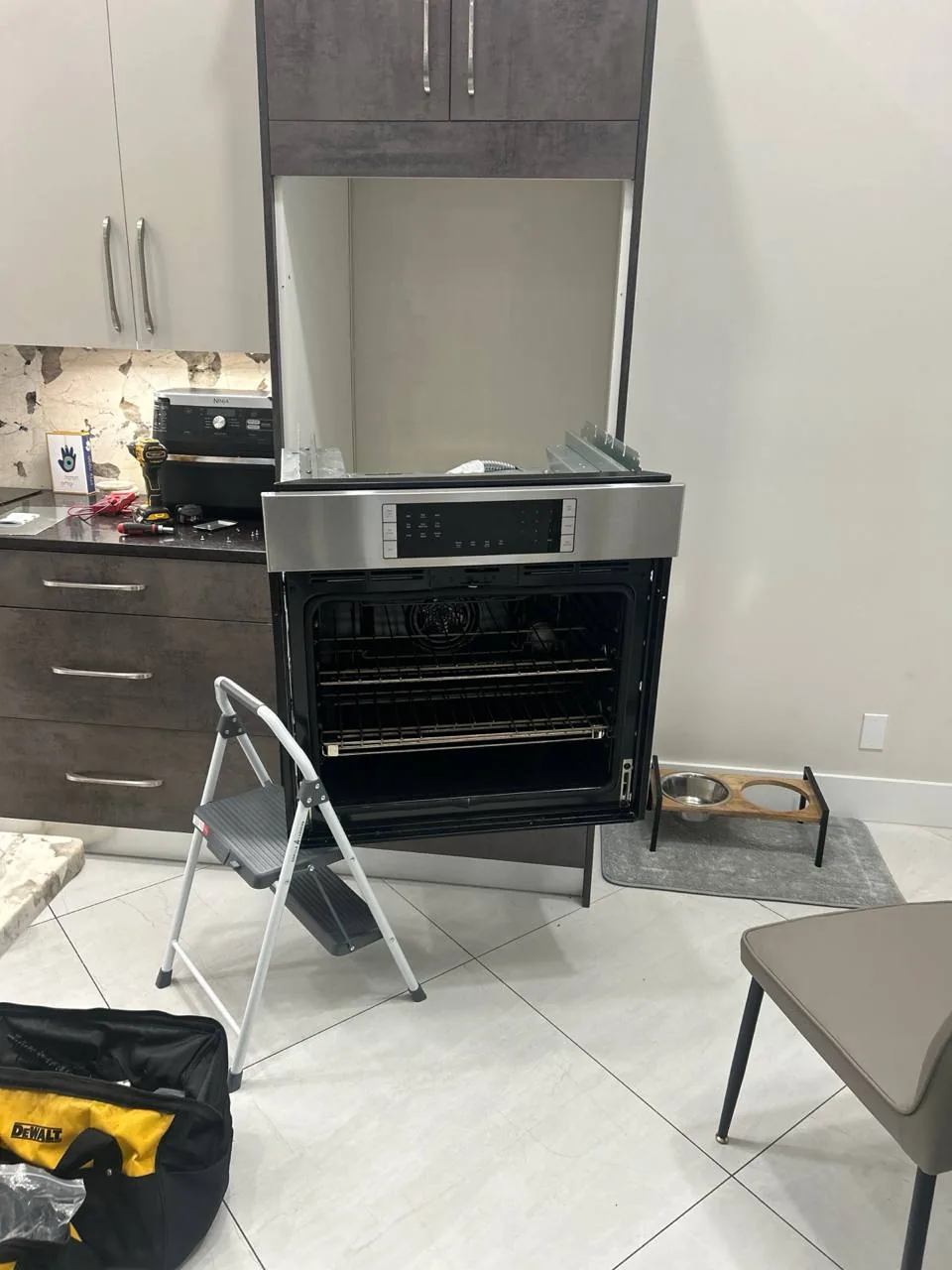 An oven being repaired, with tools, a step stool, and parts on the counter