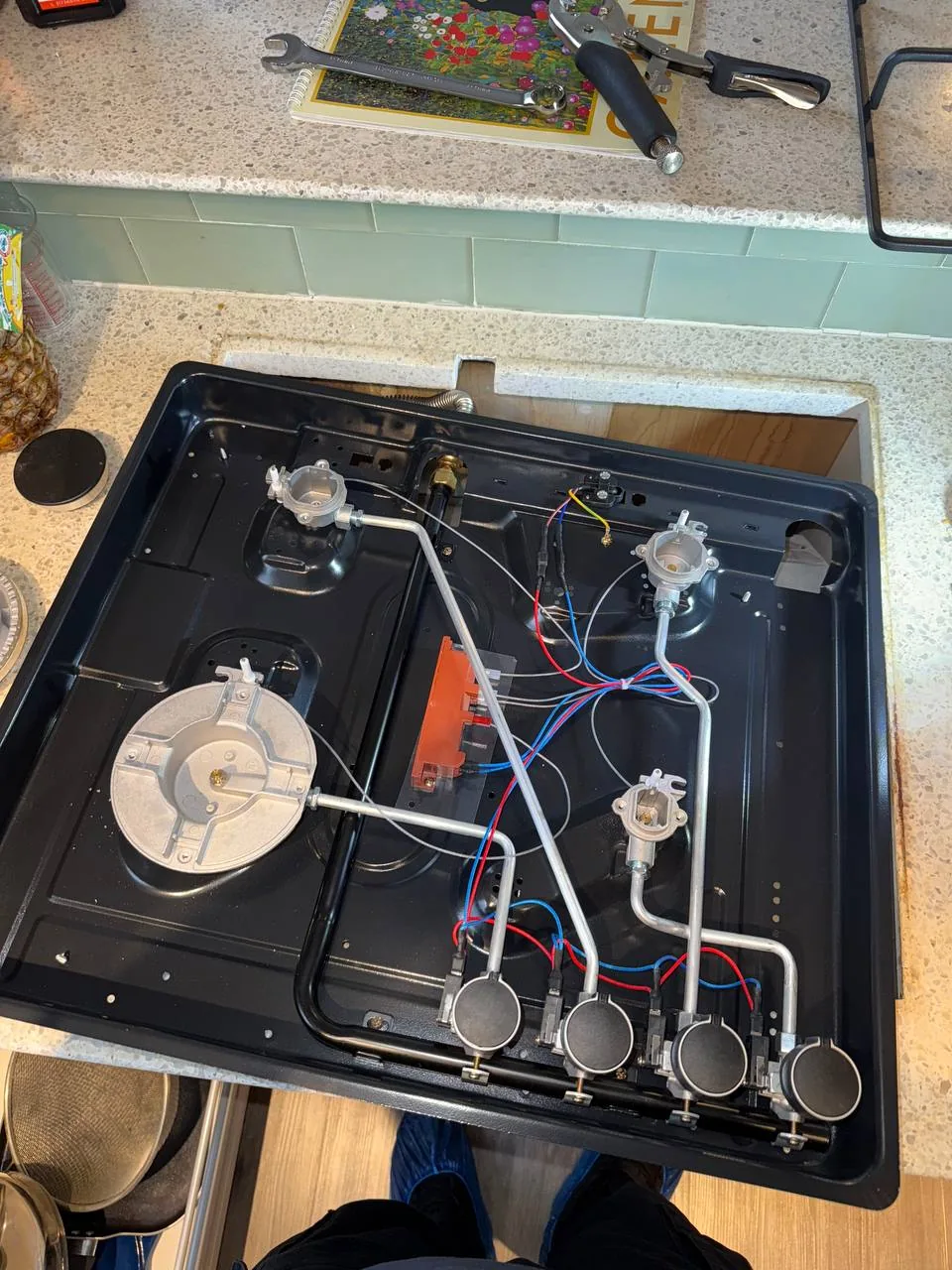 A technician is repairing a cooktop, with the internal components and wiring visible on a countertop