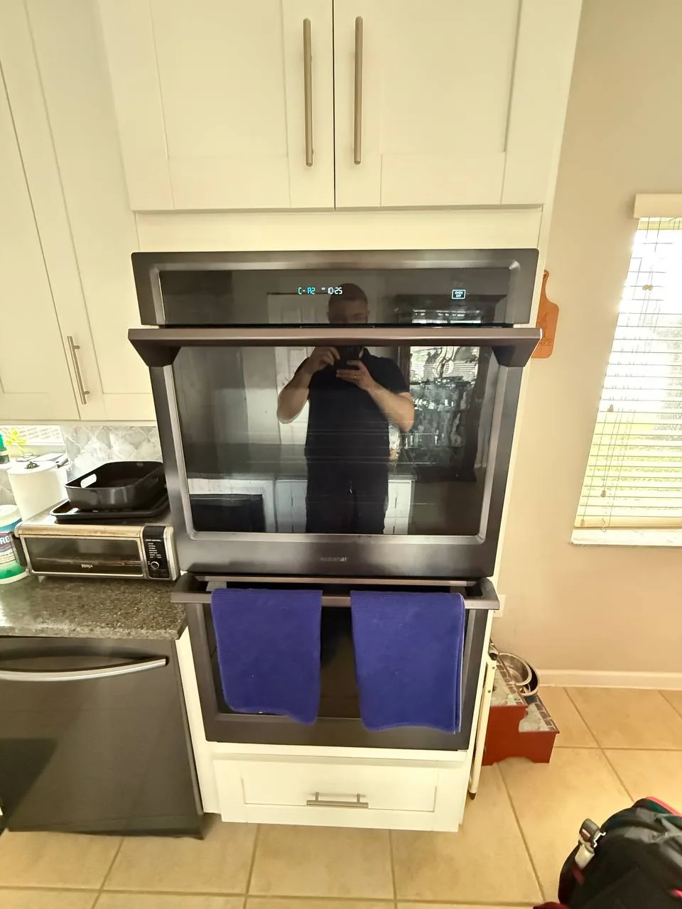 A technician is reflected in the glass of a modern built-in oven