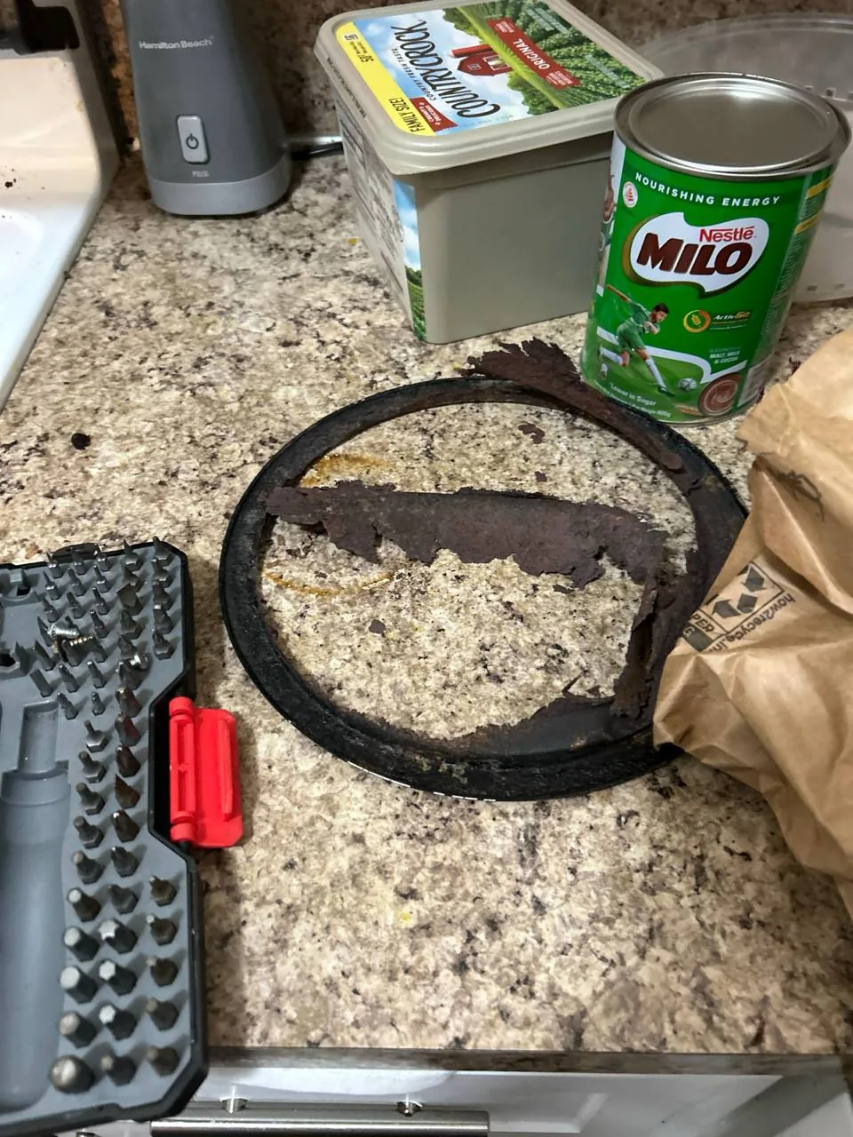A corroded heating element from a cooktop on a countertop next to a tool kit