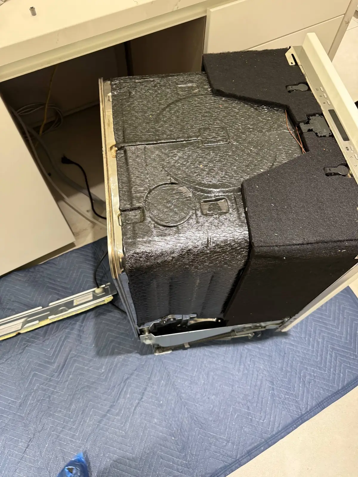 A dishwasher is pulled out from under the counter for repair, sitting on a protective mat