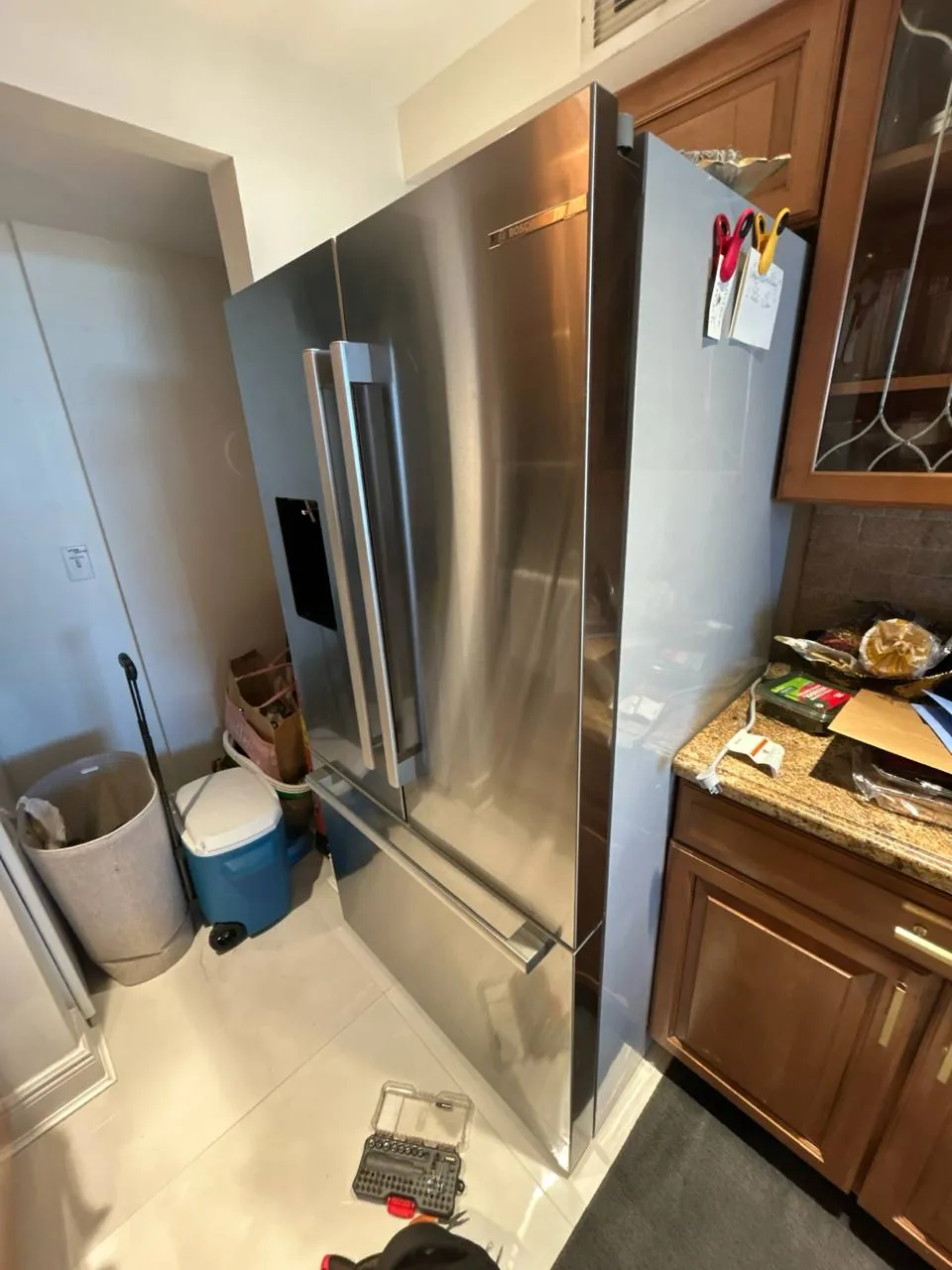 A stainless steel Bosch refrigerator in a kitchen, with tools on the floor