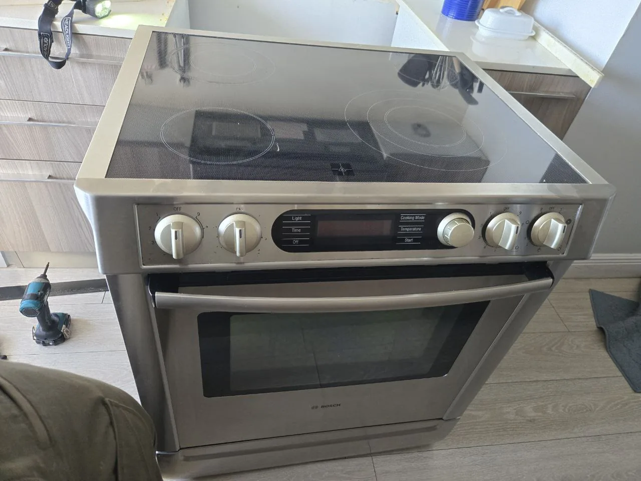 A stainless steel Bosch oven with a smooth cooktop and control panel in a kitchen setting with a technician's leg and tools