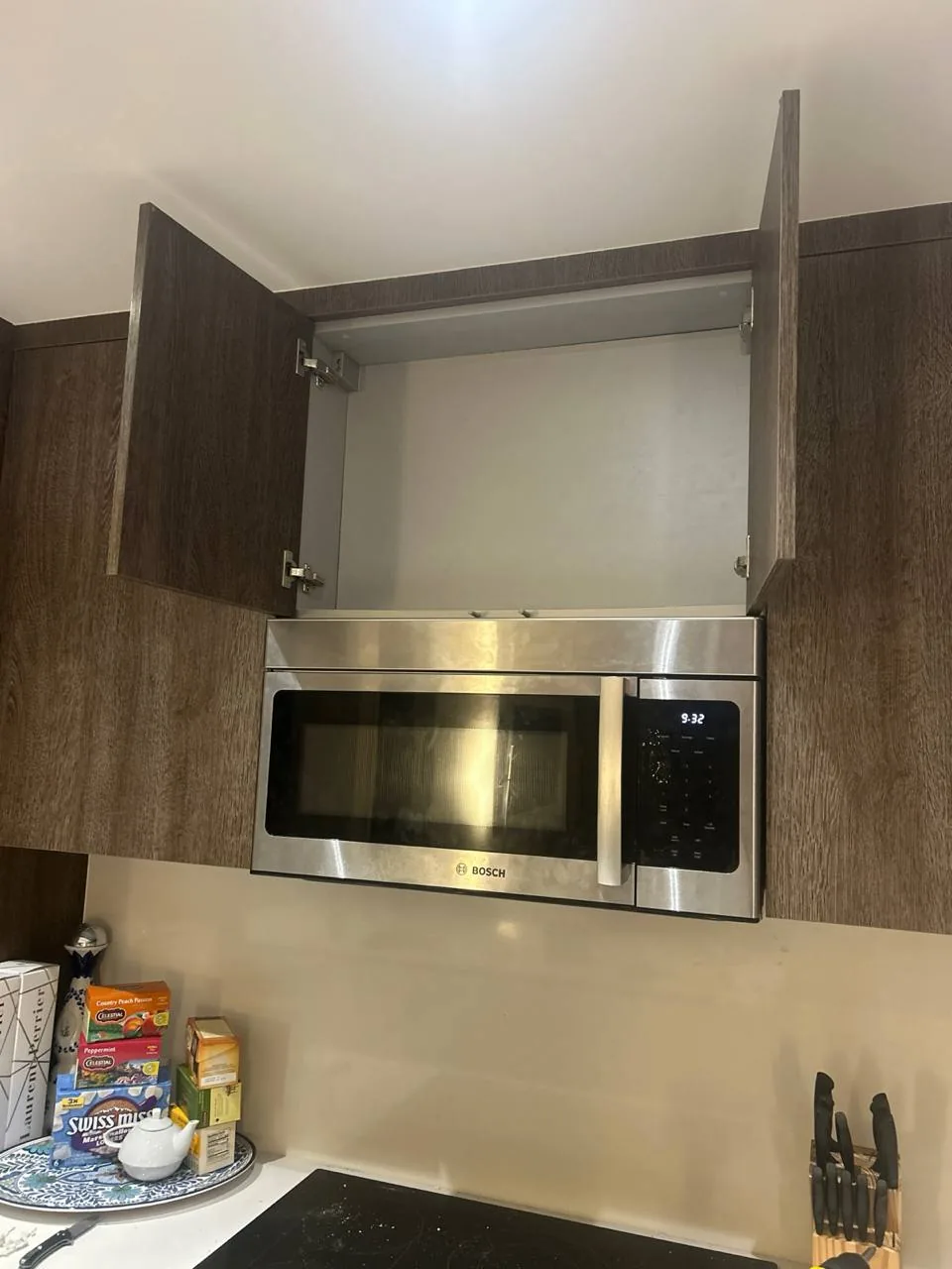 A Bosch microwave is installed above a stovetop, with kitchen cabinets above it and various kitchen items on the counter