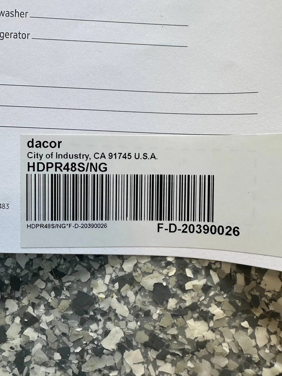 A Dacor model number label, likely for a cooktop, on a white document above a speckled floor
