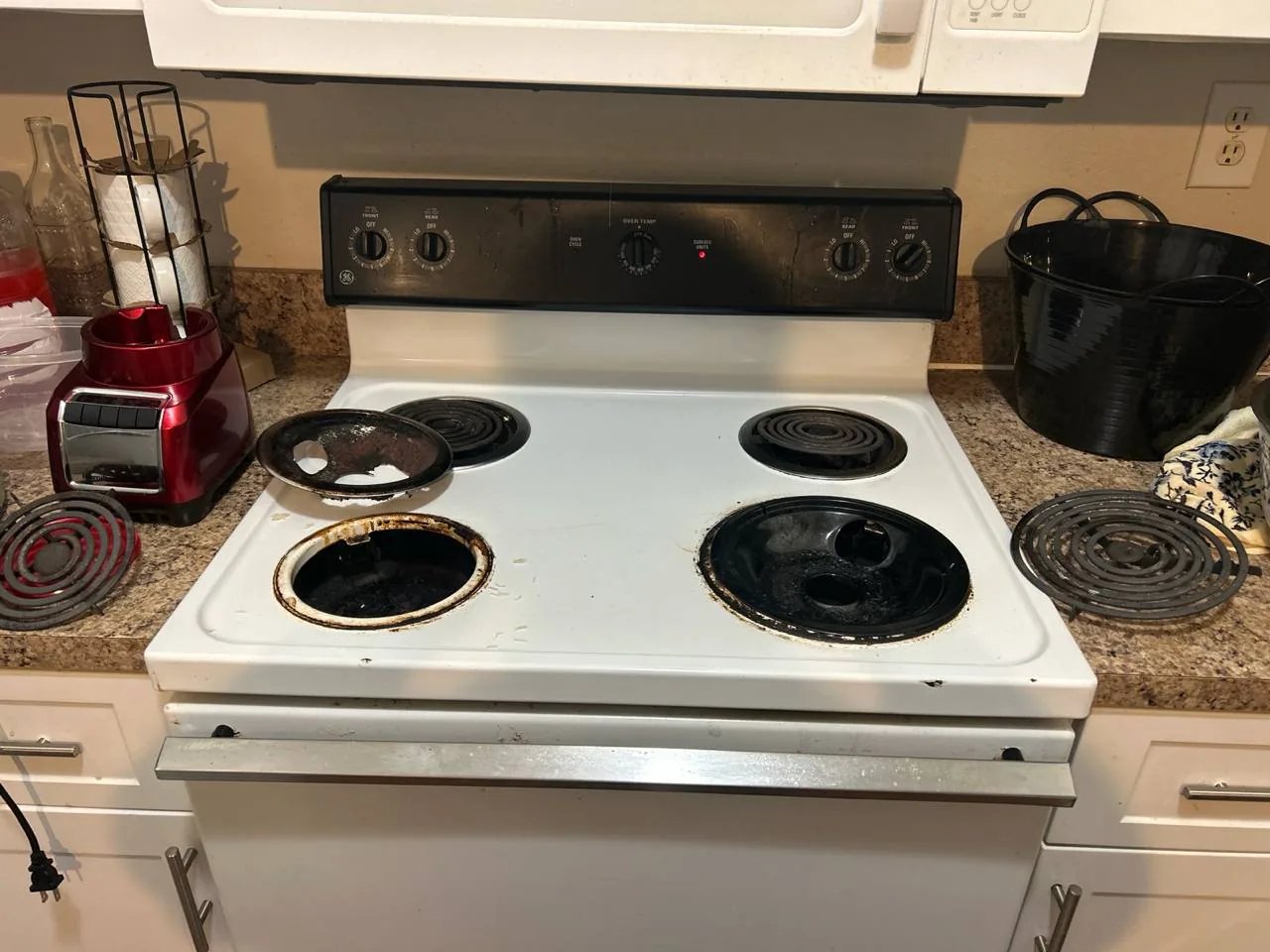 An electric oven range with removed burners and drip pans on a kitchen counter