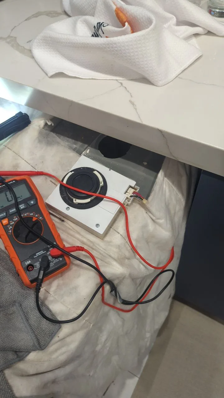 A wine cooler fan component is being tested with a multimeter on a protective mat under a countertop