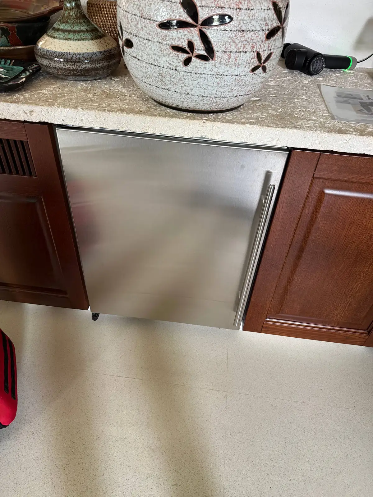 A stainless steel wine cooler installed under a counter with decorative vases on top