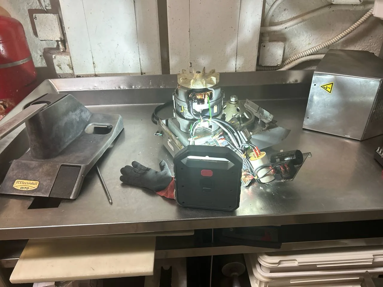 A disassembled commercial dishwasher component with 'Electrolux DITO' visible on a part, illuminated by a work light, sits