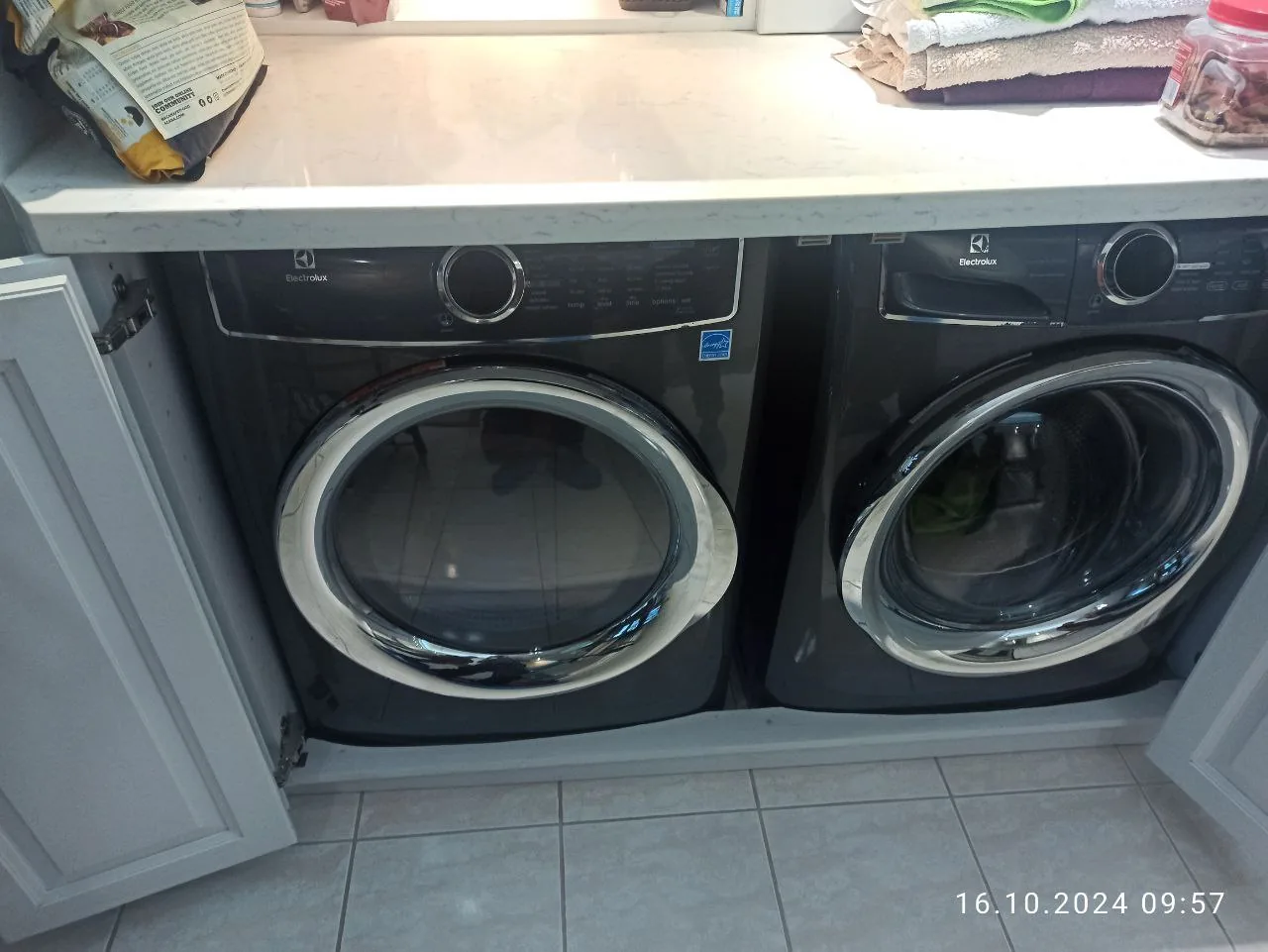 Two dark-colored Electrolux front-load washers under a white counter, with cabinets open on both sides