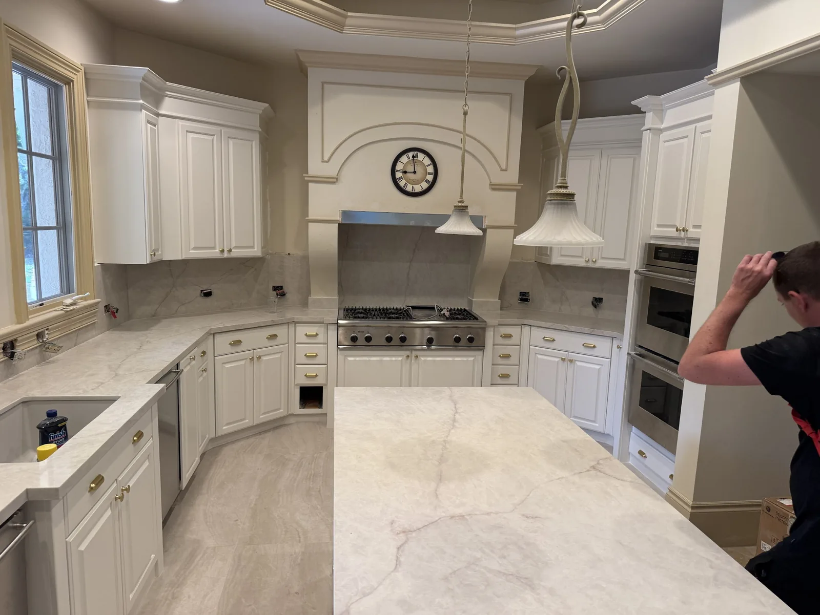A technician near a double wall oven in a modern kitchen with a large island and range