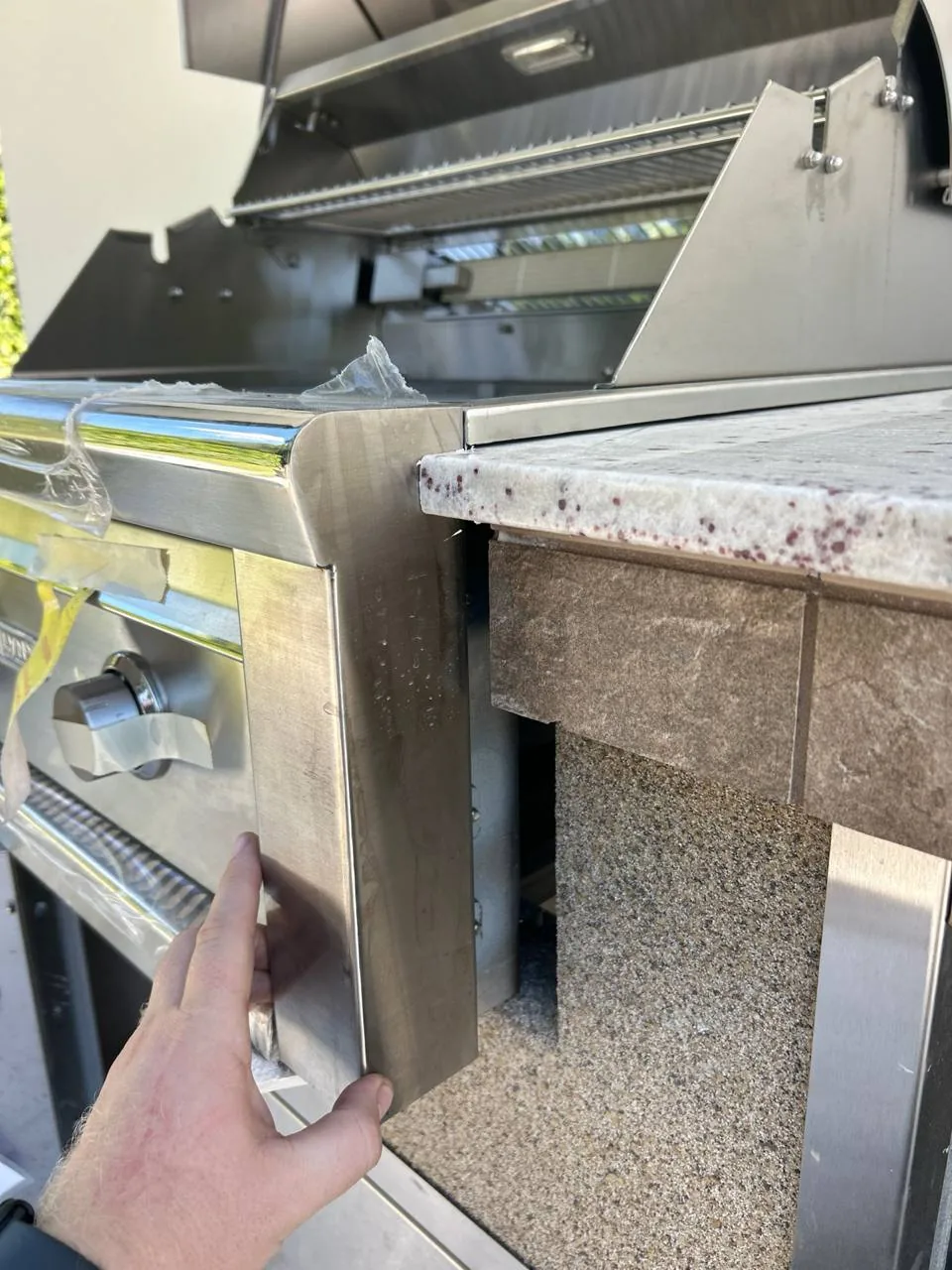 A hand installing a new stainless steel cooktop into an outdoor kitchen counter