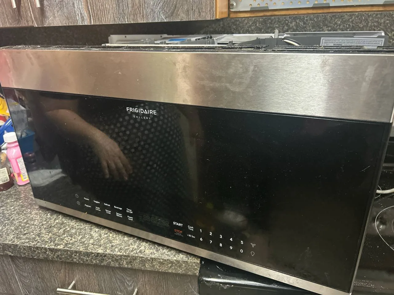 A Frigidaire Gallery microwave on a countertop, with a technician's reflection visible