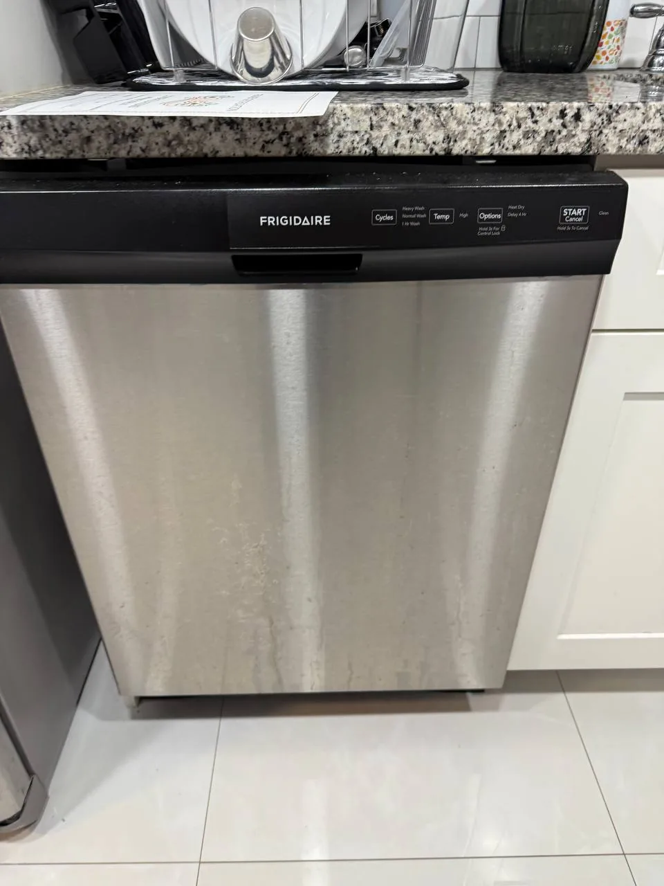 A Frigidaire dishwasher installed in a kitchen, with some water stains on its stainless steel door