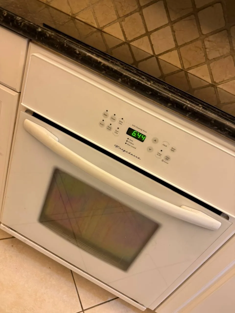 A white Frigidaire oven with a digital display showing 6:44 is installed below a dark countertop