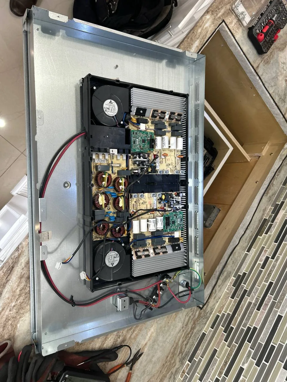 The internal components of a cooktop are exposed on a counter with tools nearby