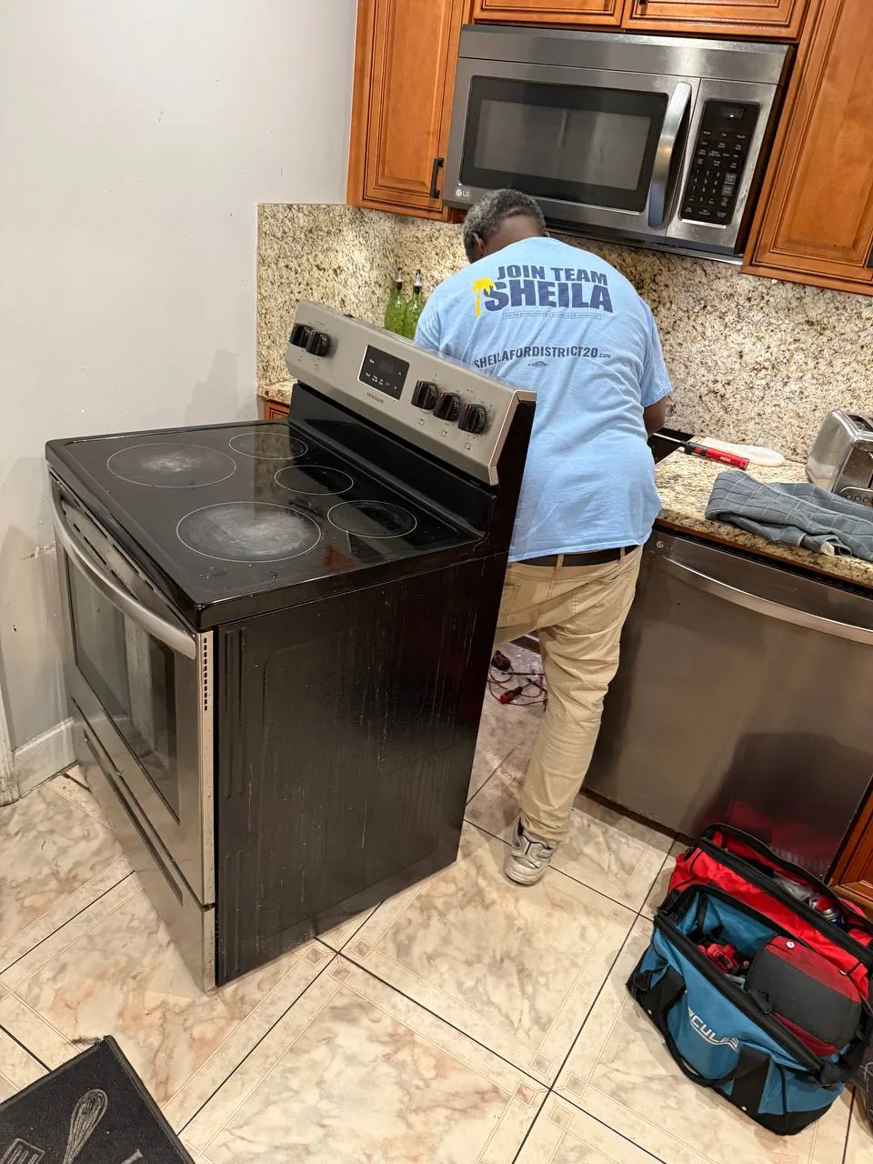 A technician is working on a stove with a microwave above it in a kitchen