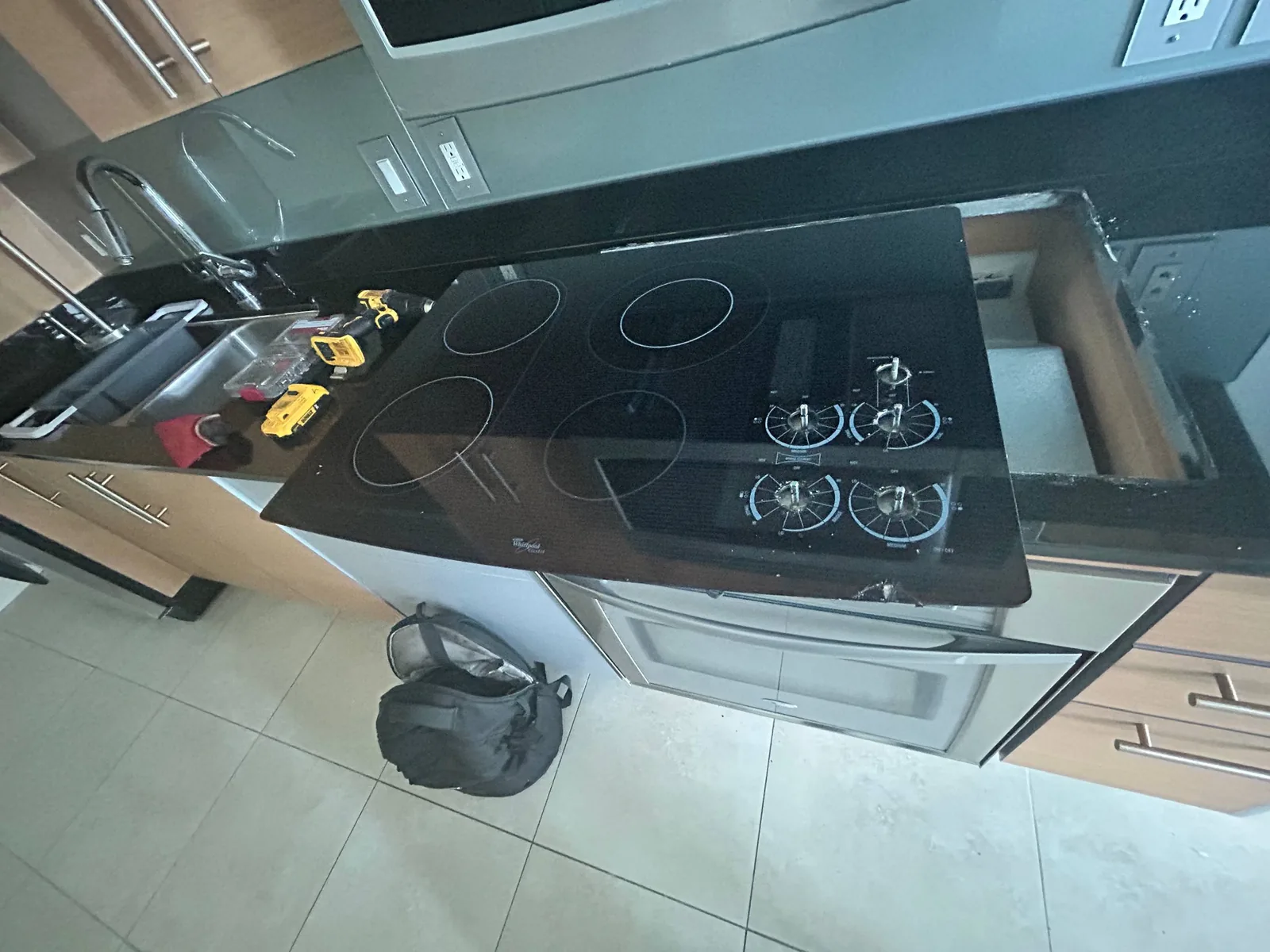 A partially installed cooktop on a kitchen counter next to a sink and tools