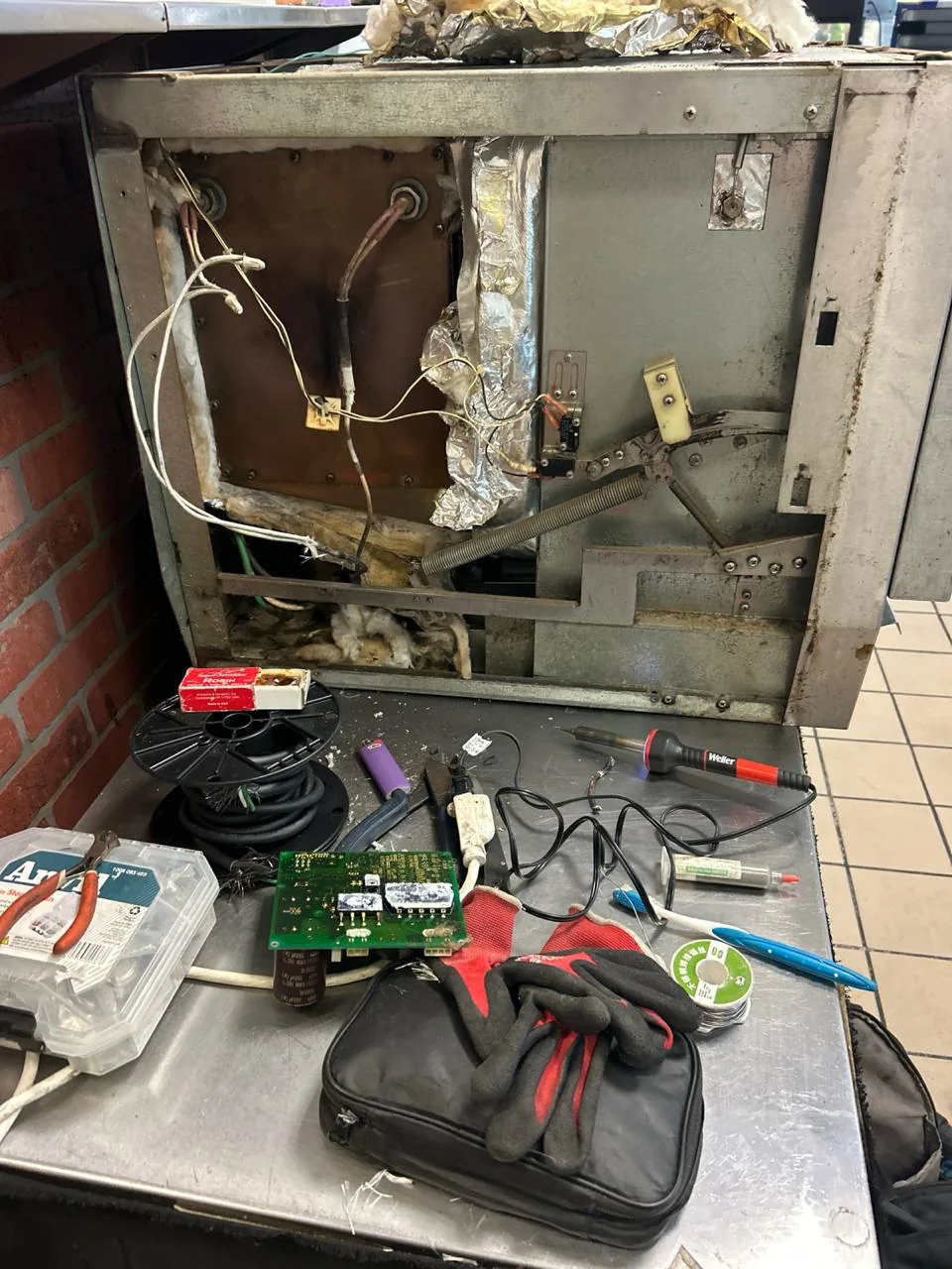 A disassembled oven and various repair tools are on a metallic table in a kitchen setting