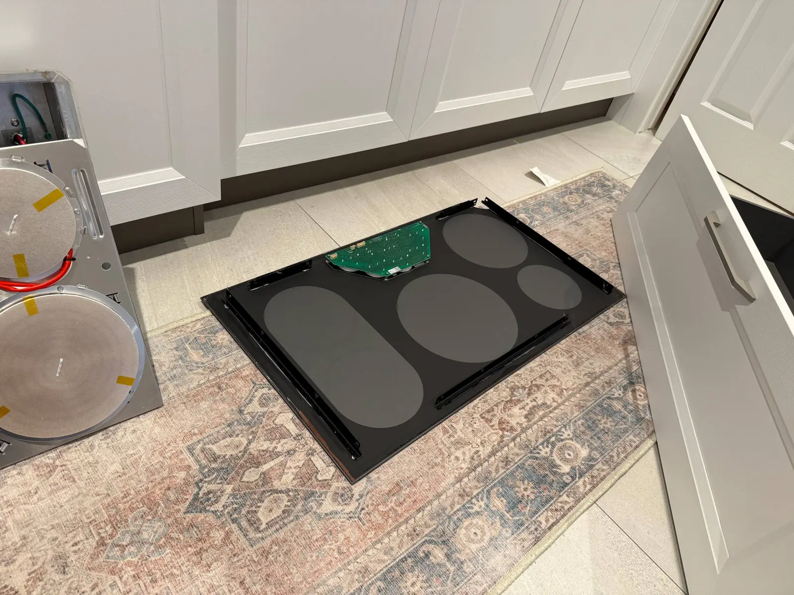 A cooktop is disassembled on a rug in a kitchen, with its components laid out