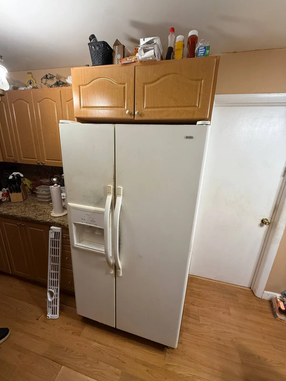 A white side-by-side refrigerator in a kitchen with its bottom front grill removed