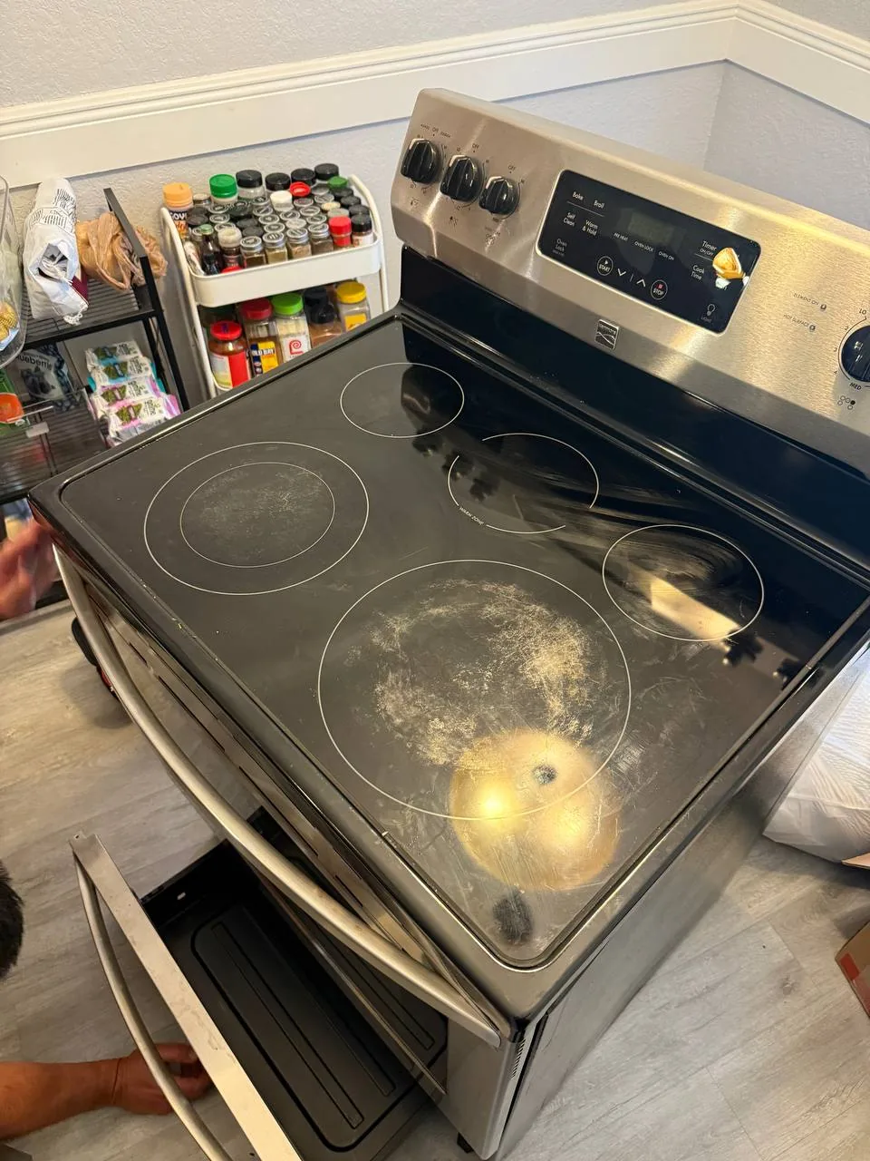 A technician working on a stainless steel oven with a glass cooktop, which appears to be pulled out from the wall