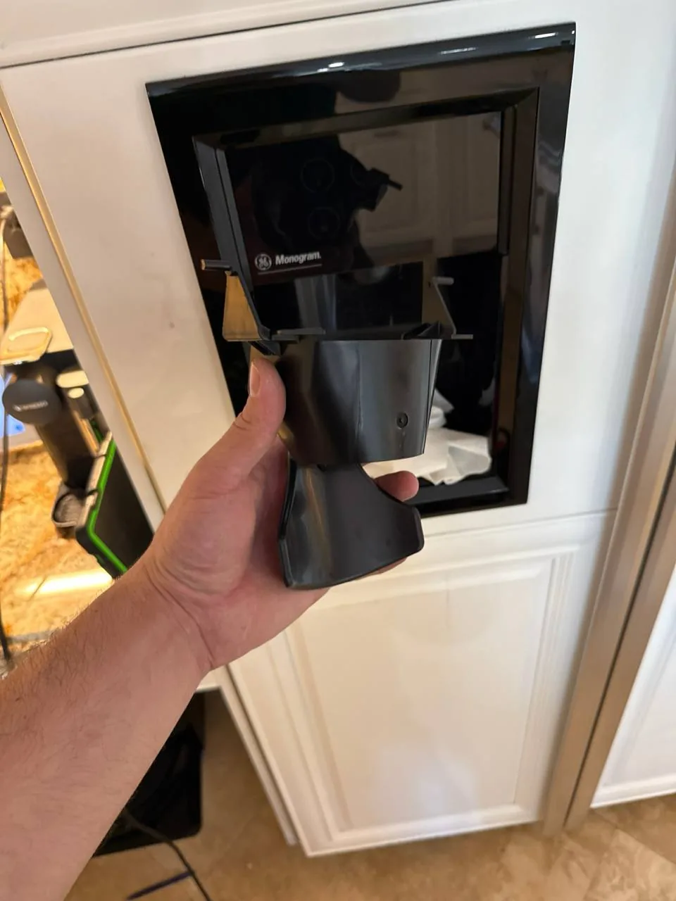 GE Monogram coffee machine service: a technician's hand is holding a part in front of a built-in Monogram coffee machine