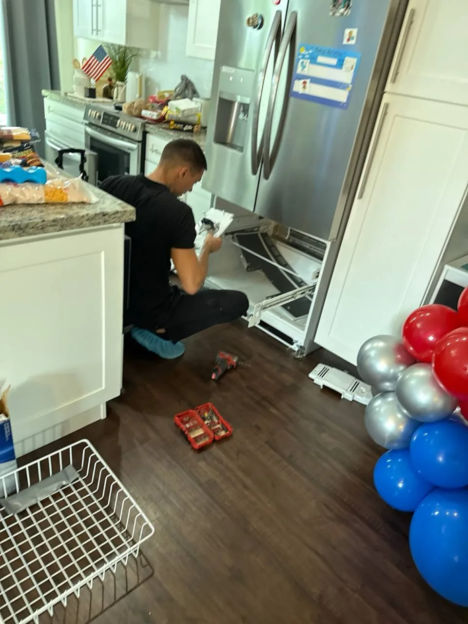 A technician is working on the lower drawer of a stainless steel refrigerator