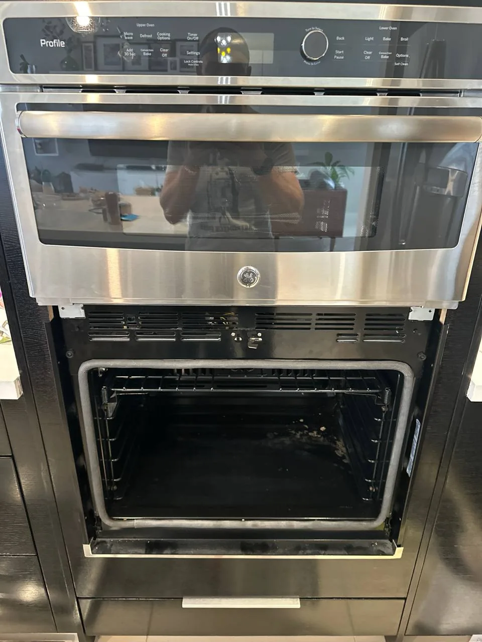 A built-in GE Profile oven and microwave unit with the oven door open, revealing the dirty interior
