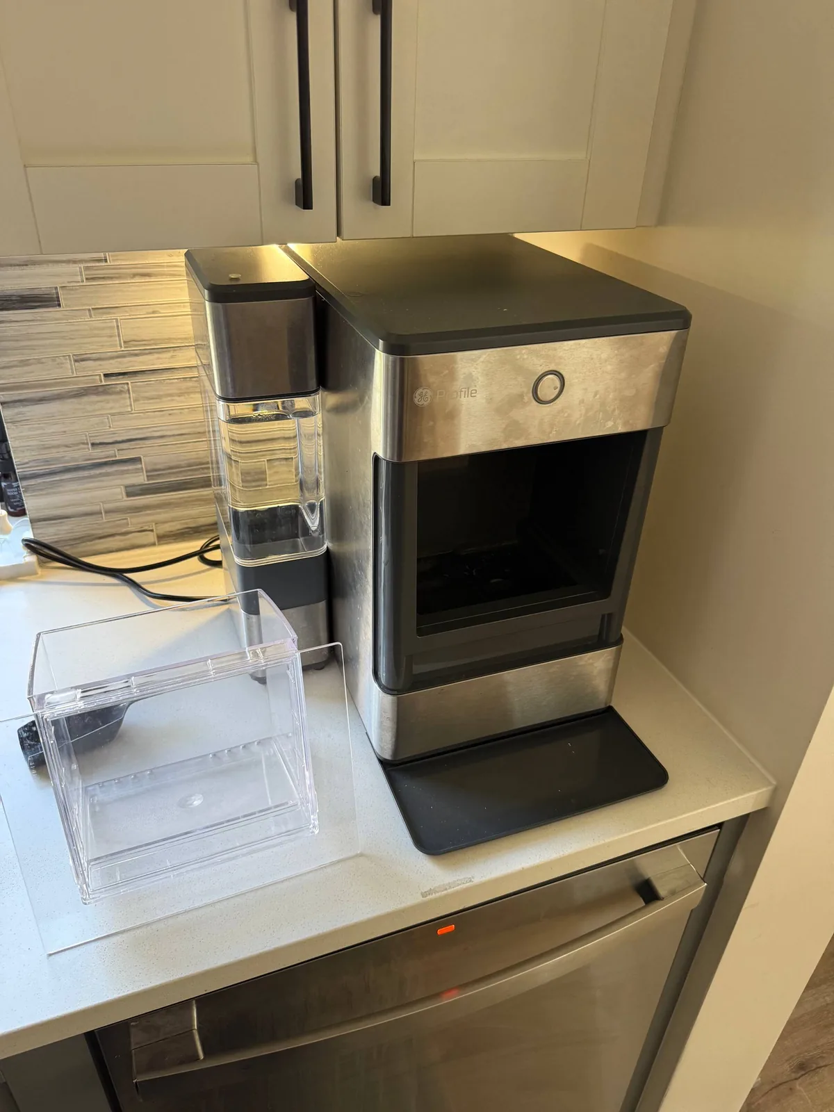 A GE Profile countertop ice maker and an empty ice bin are on a kitchen counter