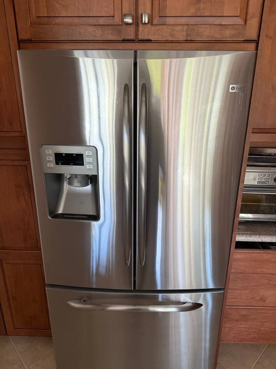 A stainless steel GE Profile refrigerator with a water and ice dispenser in a kitchen setting