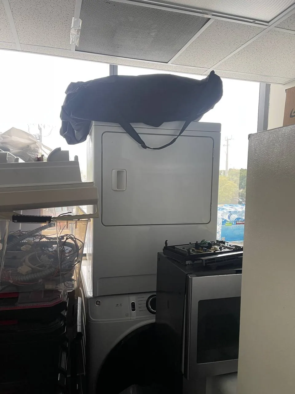 A white GE dryer is stacked on top of a washer, with a partially disassembled microwave and clear plastic bins of wires