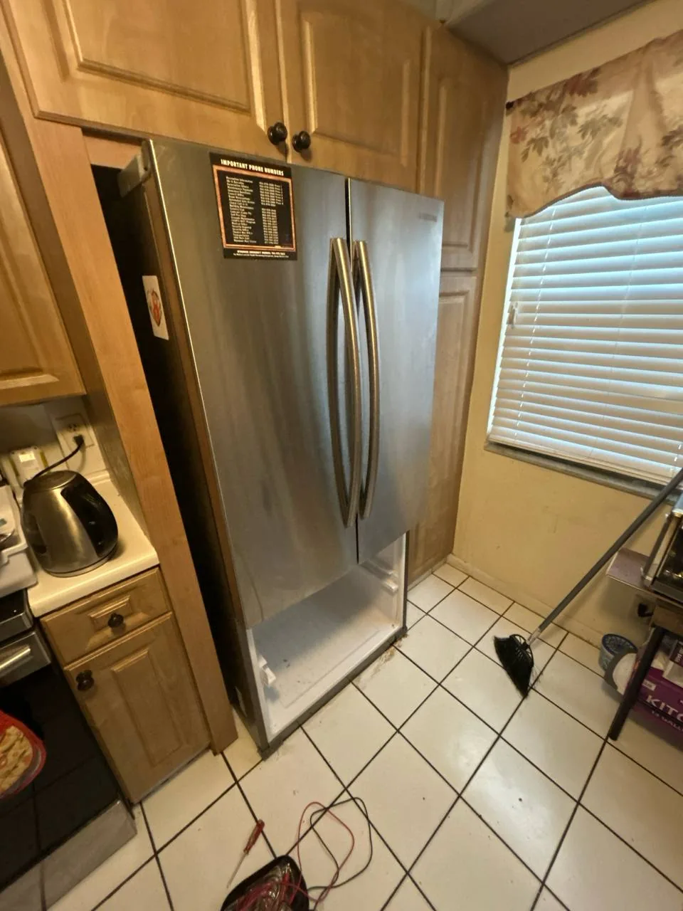 A stainless steel French door refrigerator with its bottom freezer drawer open, tools on the floor nearby
