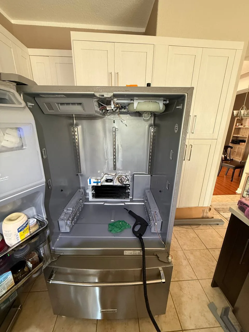 A stainless steel refrigerator with its interior disassembled for repair, showing internal components and a steamer tool