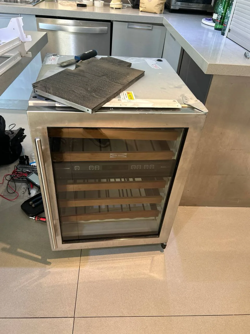 A wine cooler with its top panel removed, and tools are nearby on the counter