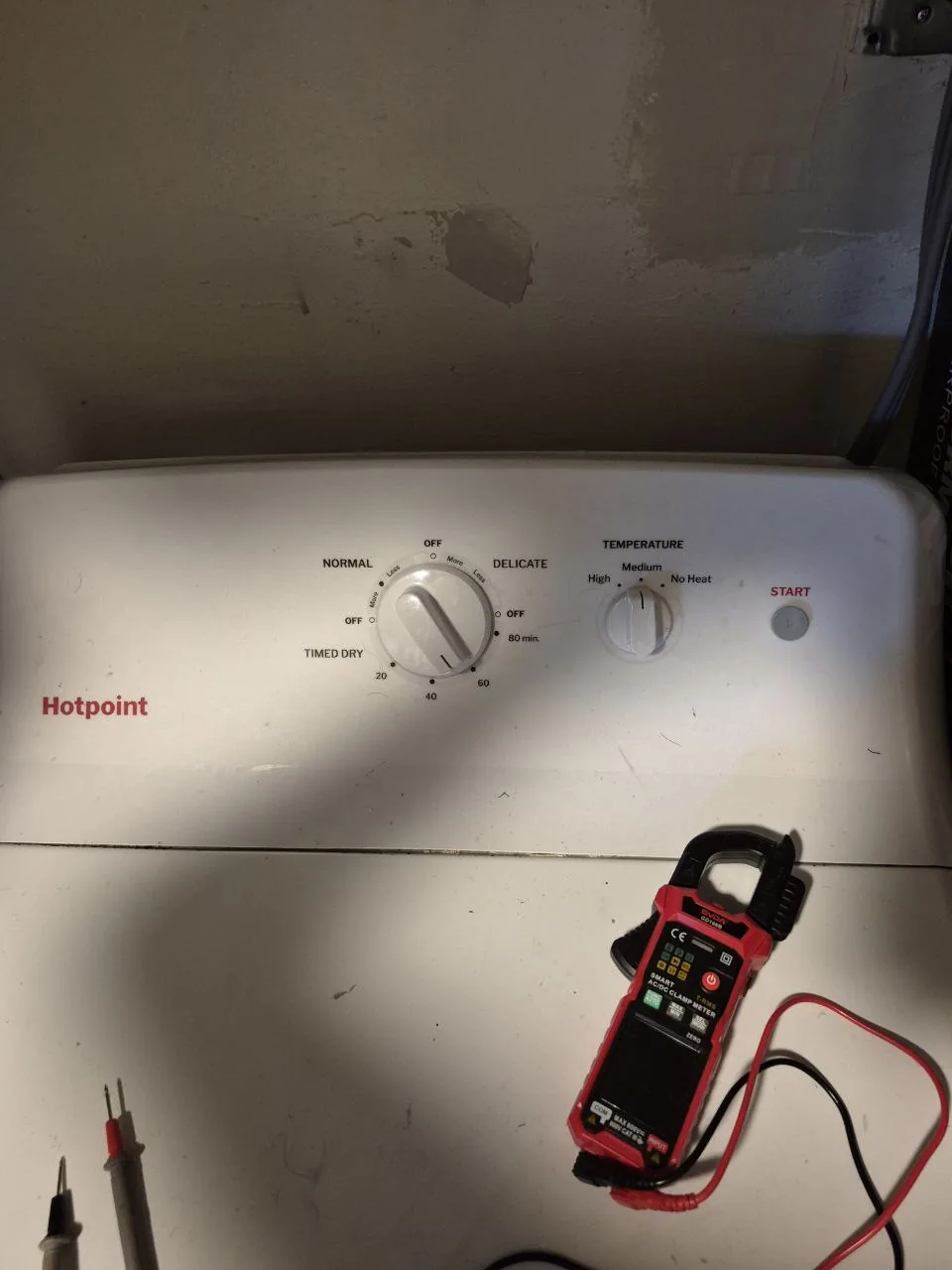 A Hotpoint dryer control panel with a clamp meter on top