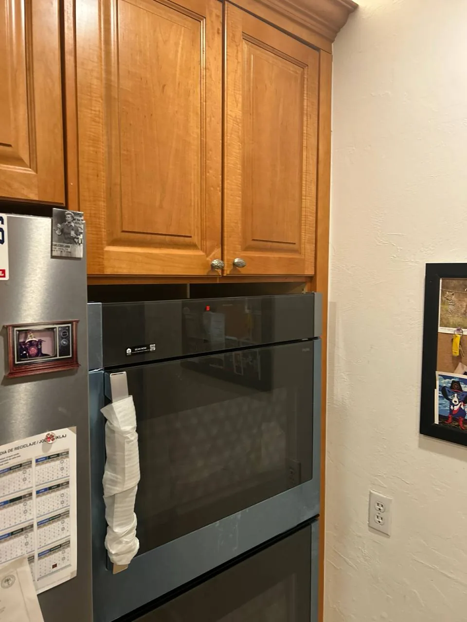 A new oven is installed in a kitchen with wooden cabinets and a refrigerator to the left